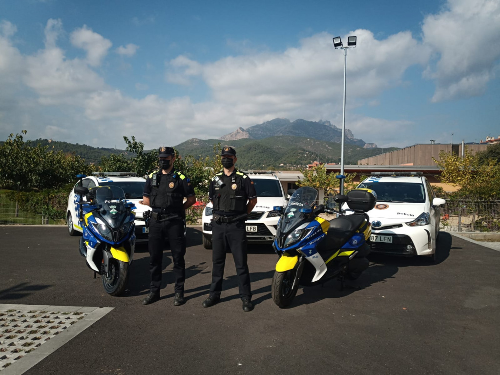 Dos agents davant de tres cotxes de policia i amb les seves motos al costat