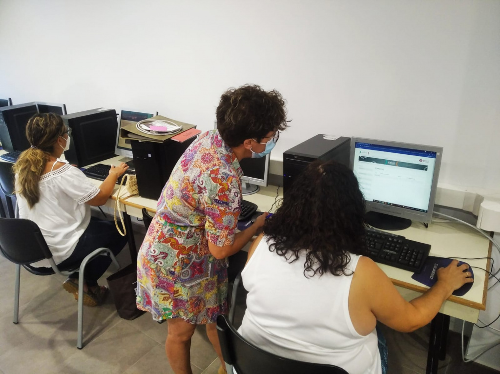 Sala amb ordinadors i dues usuàries reben suport d'una orientadora laboral